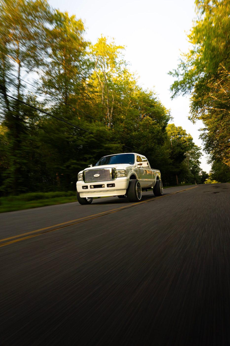 White Ford Super Duty truck rolling down a tree-lined road
